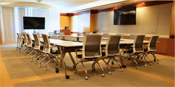 Orbach 240 conference room set up conference or boardroom style, with tables arranged in a long rectangle surrounded by chairs and two wall-mounted monitors.