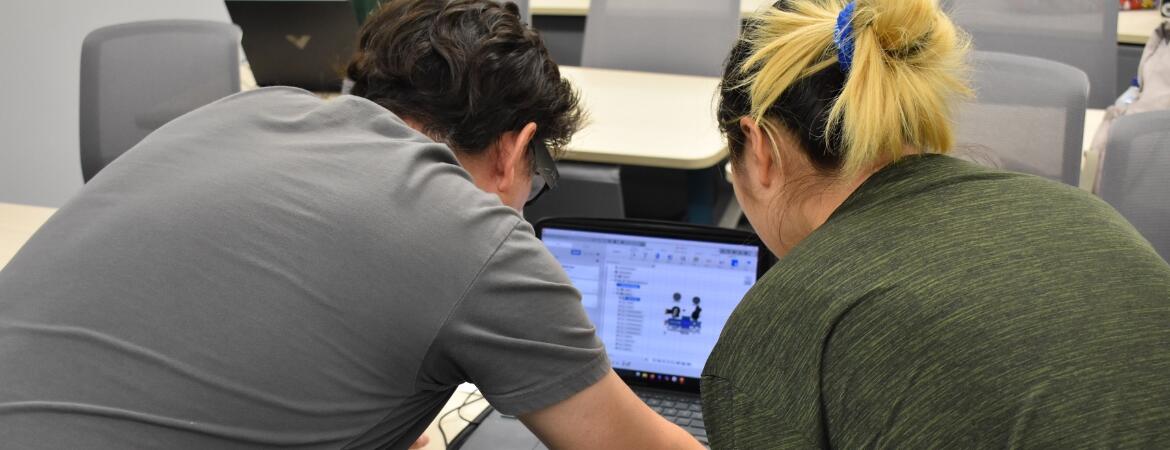 Image of Innovative Media Librarian Alvaro Alvarez (left) and a robotics camps student looking at the computer