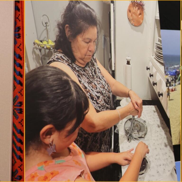 Three images from the Semana de la Mujer exhibit at Tomás Rivera Library: a black-and-white portrait photograph of a young woman from 1958 set against a colorful woven textile border; a color photograph of an older woman teaching a young girl at a kitchen counter; and an illustrated lotería-style card numbered 8, depicting a crowned woman holding a baby, titled 'La Hermana Mayor'.