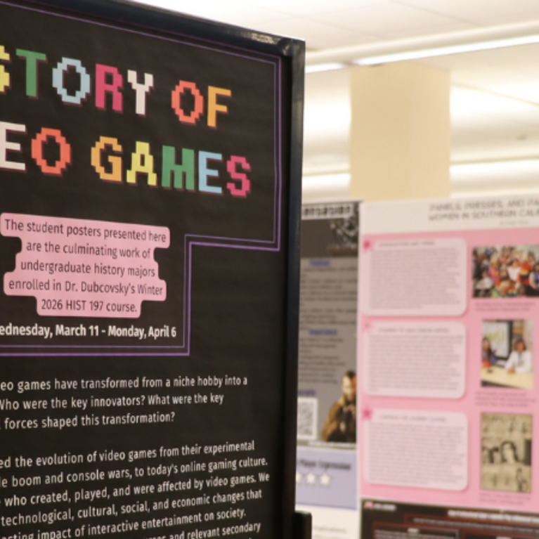 This exhibition, titled "History of Video Games," showcases student research posters from Dr. Dubcovsky’s Winter 2026 HIST 197 course. The display features a prominent pixel-art sign explaining the course's focus on the cultural evolution of gaming, with the exhibition running from March 11 to April 6.