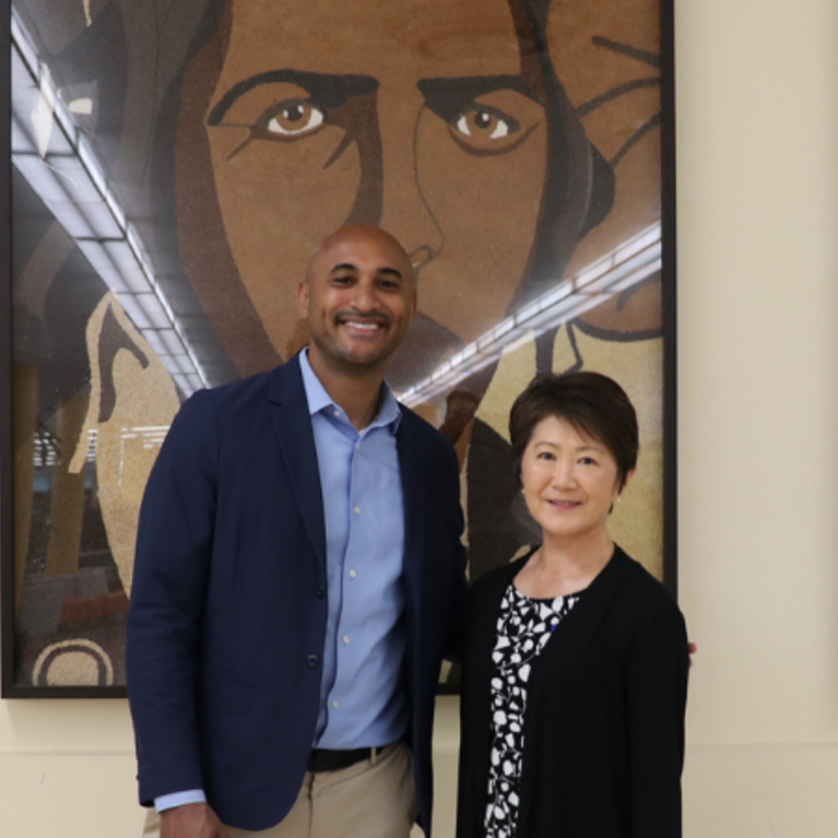 Congressman Shomari C. Figures and University Librarian Mihoko Hosoi standing together inside the UCR Tomás Rivera Library in front of three large paintings of Tuskegee Airmen, originally featured on a 2010 Rose Parade float.