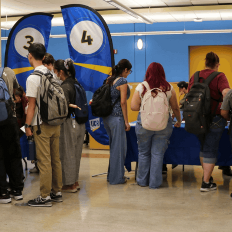 Student attending the 2026 Library Open House in Rivera Library, blur flags in the background indicate stations where students are gathered.
