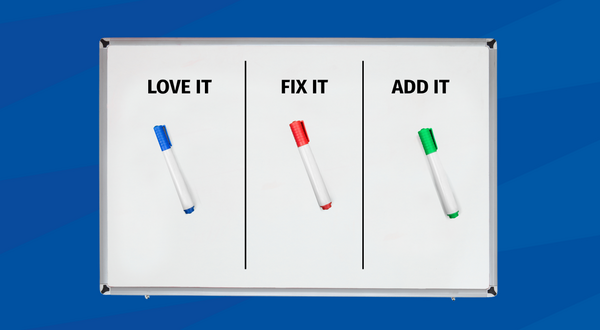 A whiteboard with a silver frame is centered on a blue geometric background. The board is divided into three vertical columns labeled "LOVE IT," "FIX IT," and "ADD IT," with a corresponding blue, red, and green dry-erase marker in each section.