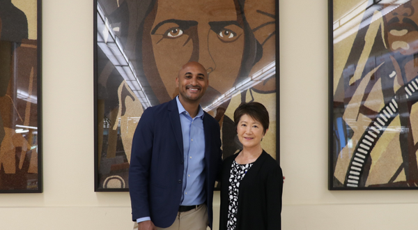 Congressman Shomari C. Figures and University Librarian Mihoko Hosoi standing together inside the UCR Tomás Rivera Library in front of three large paintings of Tuskegee Airmen, originally featured on a 2010 Rose Parade float.