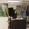  Laila Lalami reads at a podium in front of the "Neon in the Gutters: Cyberpunk Visions of the Future" exhibition display.