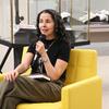  Laila Lalami speaks into a microphone while seated in a yellow armchair, holding a copy of The Dream Hotel.
