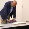 Congressman Shomari Figures leaning over a table, closely observing a historical document.