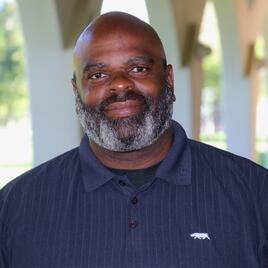 Ken Tracey headshot photo outside of RIvera Library under the arches. 